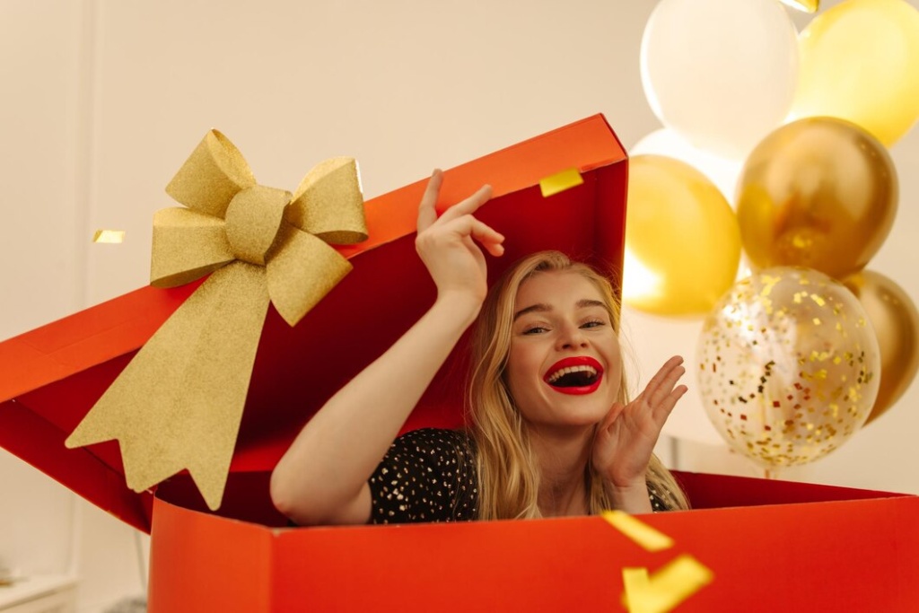 joyful-fairskinned-young-blonde-enthusiastically-climbs-out-large-red-box-as-surprise-holiday-concept_197531-31792.jpg